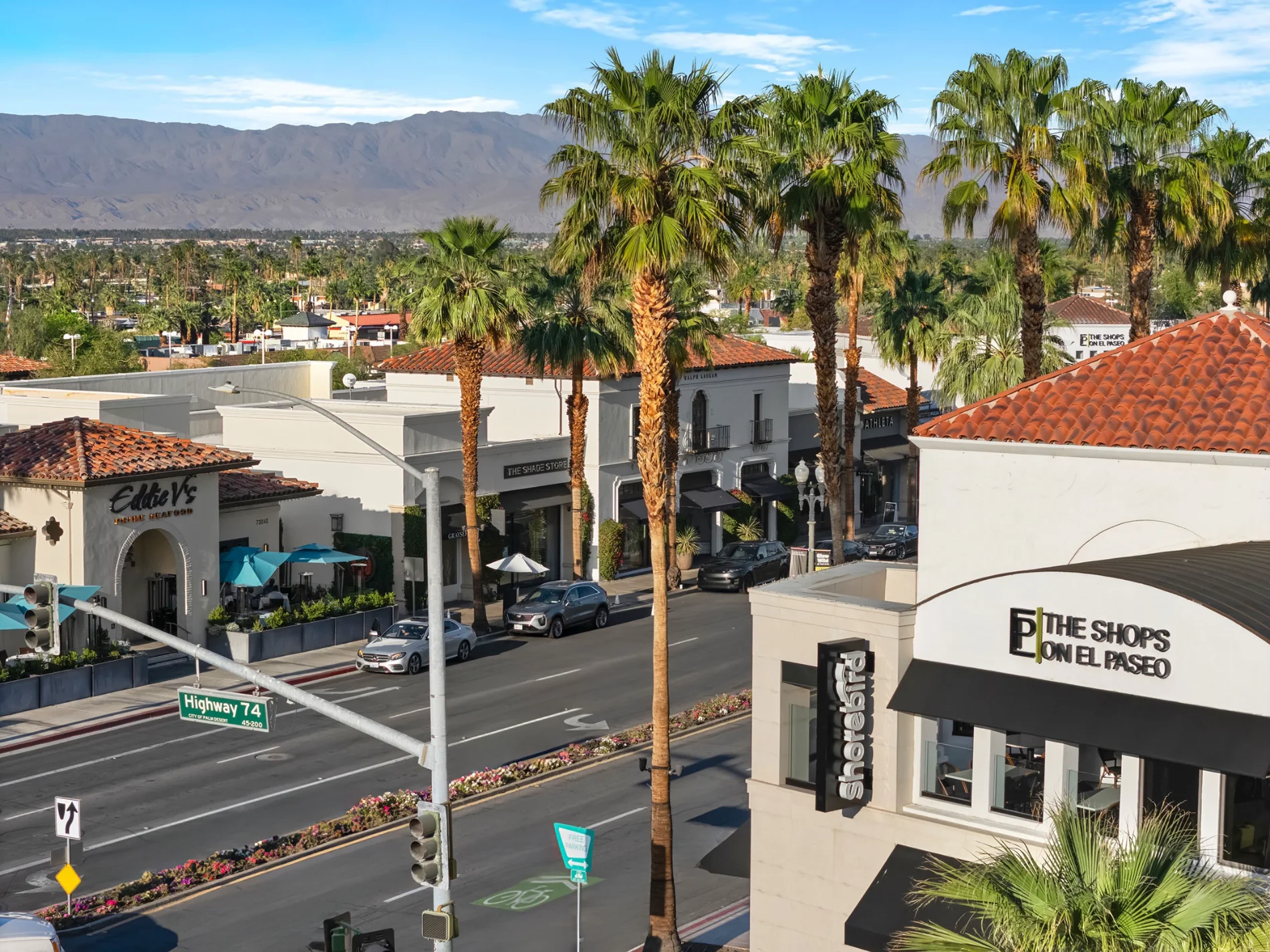 El Paseo from above: storefronts, palms and The Shops on El Paseo signage with the Santa Rosa Mountains beyond