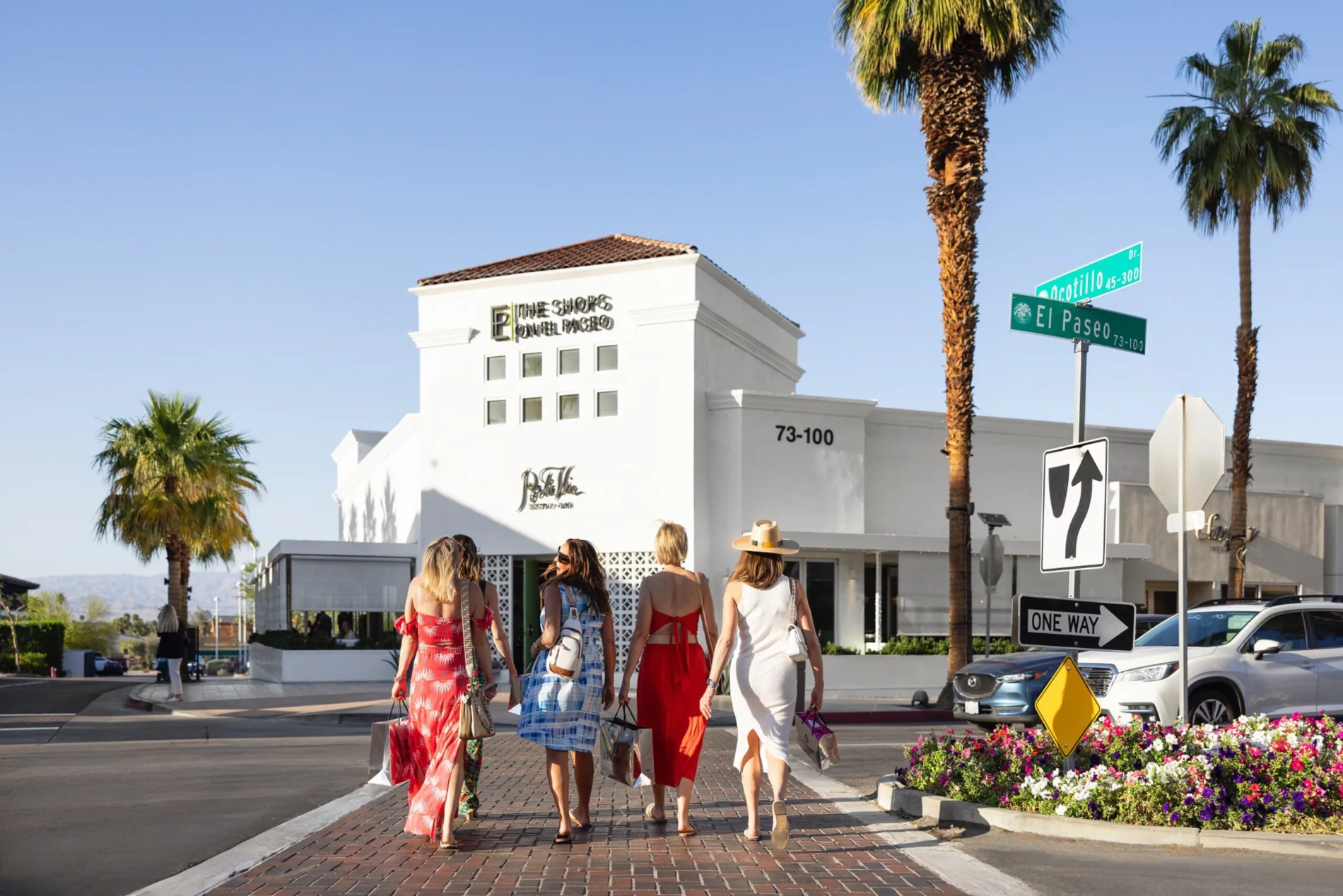 Five women with shopping bags crossing El Paseo toward The Shops on El Paseo, palms overhead